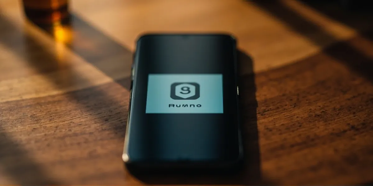 A smartphone displaying a rummy app icon on a wooden desk in warm natural light.
