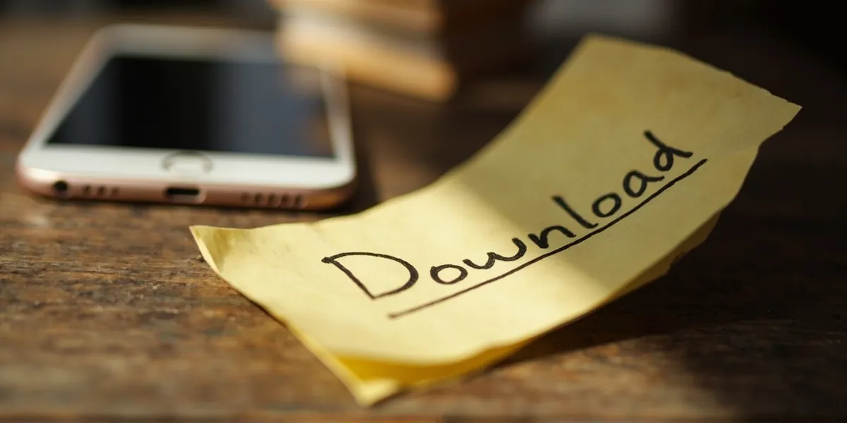 A paper note reading 'Download' handwritten beside a smartphone on a wooden desk.